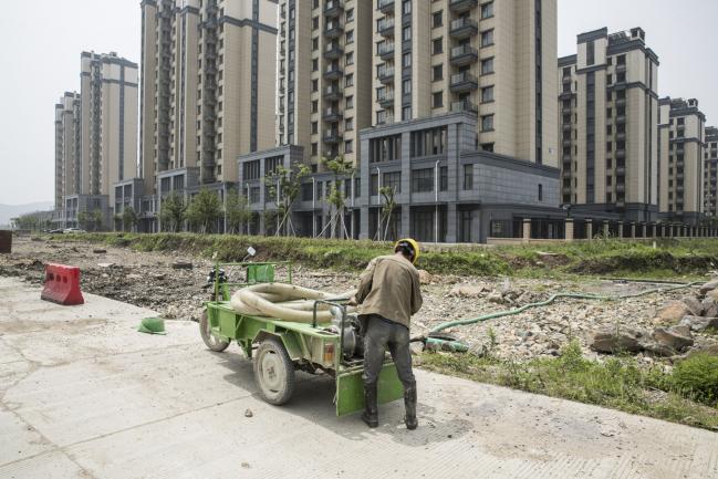 © Bloomberg. A construction worker stands in front of new residential apartments on the outskirts of Yuyao, China, on Monday, May 28, 2018. Yuyao is home to Sunny Optical Technology Group, a lens maker founded more than three decades ago by a former appliance-factory worker with a high school education and less than $10,000 of borrowed cash, and is now a $22 billion behemoth that supplies lenses to the likes of Samsung and Xiaomi. Photographer: Qilai Shen/Bloomberg