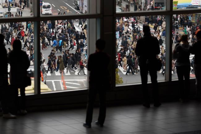 © Bloomberg. People are silhouetted as they stand on a footbridge overlooking pedestrians crossing an intersection in the Shibuya district of Tokyo. Photographer: Akio Kon/Bloomberg