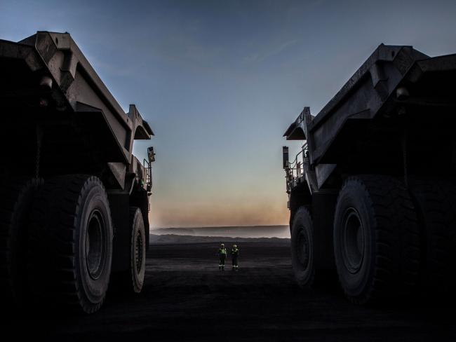 © Bloomberg. Workers stand near dump trucks at a mine. 