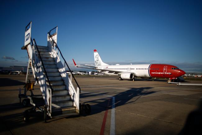 © Bloomberg. A mobile passenger boarding stairway stands parked near to a passenger aircraft operated by Norwegian Air Shuttle AS at London Gatwick airport in Crawley, U.K.