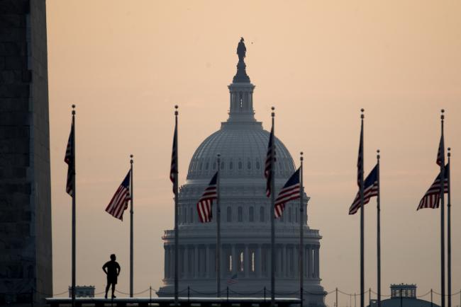 © Bloomberg. The U.S. Capitol building stands past a runner pausing at the Washington Monument in Washington, D.C.