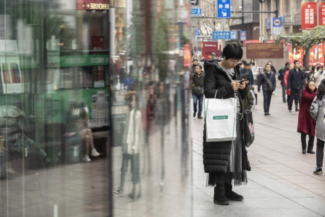 © Bloomberg. A pedestrian looks at her smartphone while standing outside an Apple Inc. store in Shanghai, China, on Tuesday, Jan. 29, 2019. Since Apple shook investors in early January with a warning, a picture is starting to emerge on where the tempering of China's $12.2 trillion economy will hurt in the coming year. Photographer: Qilai Shen/Bloomberg