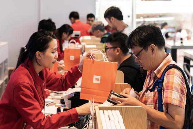© Bloomberg. An employee, left, hands a Xiaomi Corp. branded shopping bag to a customer inside a Xiaomi store in Hong Kong, China, on Friday, July 6, 2018. The tussle over Xiaomi's high valuation and concern over a U.S.-China trade war have overshadowed what had been one of the world's most highly-anticipated initial public offerings of the year. Photographer: Anthony Kwan/Bloomberg