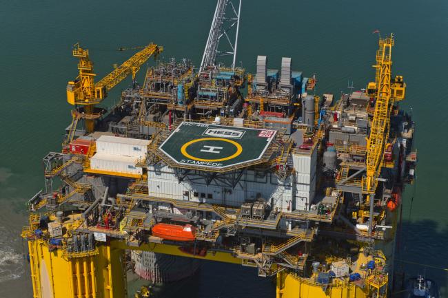 © Bloomberg. The Hess Corp. Stampede tension leg oil platform, towed from Kiewit Offshore Services Ltd., sails past in this aerial photograph taken above Ingleside, Texas, U.S., on Friday, May 5, 2017. The Stampede deepwater oil and gas field is one of the largest undeveloped fields in the Gulf of Mexico, sitting 115 miles south of Fourchon, Louisiana.