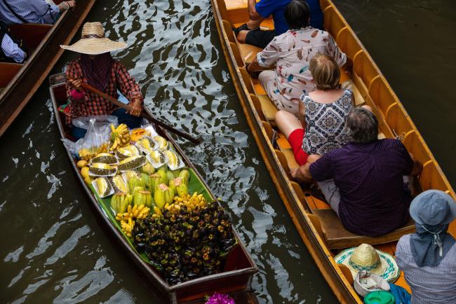 © Bloomberg. A vendor selling fruits paddles past tourists sitting on a sampan in a canal past at a floating market in Damnoen Saduak, Thailand, on Saturday, May 11, 2019. Thailand is scheduled to release first-quarter gross domestic product (GDP) figures on May 21. Photographer: Eduardo Leal/Bloomberg