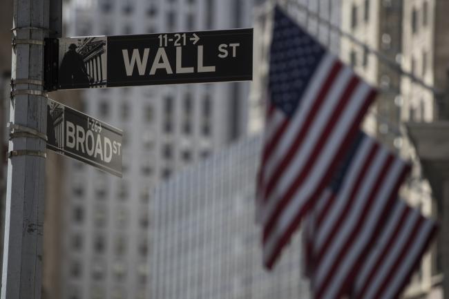 © Bloomberg. A Wall Street sign hangs in front of American flags outside the New York Stock Exchange (NYSE) in New York, U.S., on Monday, July 31, 2017. U.S. stocks fluctuated to end a month of gains spurred by corporate results and growing optimism in the strength of the global economy.