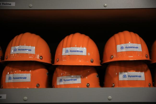 © Bloomberg. The Thyssenkrupp AG logo sits on hardhats in the visitors center at the company's metals plant in Duisburg, Germany, on Thursday, March 7, 2019. Tata Steel Ltd. is likely to offer parts of its European packaging activities to receive regulatory approval for a planned joint venture with Thyssenkrupp, Reuters reports, citing three unidentified people familiar with the matter. 