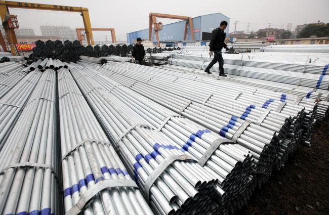 © Bloomberg. A worker walks on stacks of steel pipes at a storage yard in Shanghai, China.