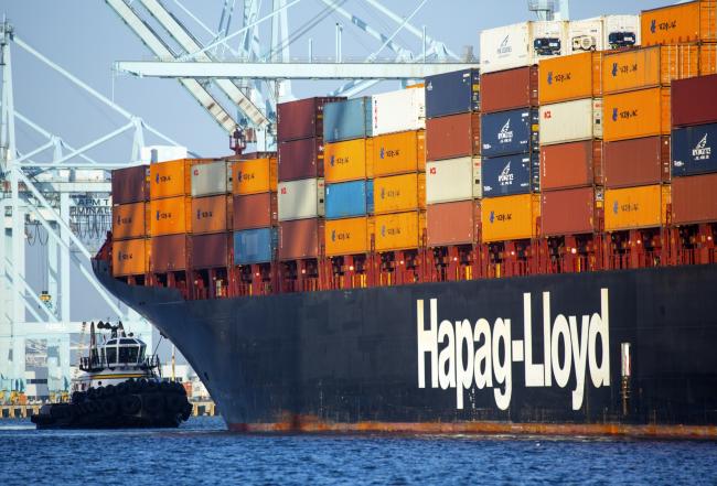 © Bloomberg. A tug boat moves into position behind a Hapag-Lloyd AG container ship at the Port of Los Angeles in Los Angeles, California, U.S., on Thursday, May 23, 2013. Maersk Line, which controls about 15 percent of global seaborne capacity, reduced its 2014 forecast for global container shipping demand growth to two percent from four percent in a report last week.