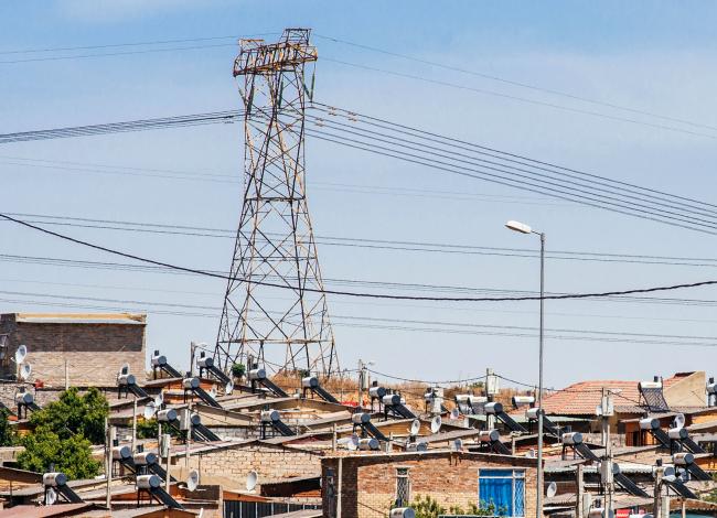 © Bloomberg. A pylon tower carries electrical power lines over residential shacks, some equipped with solar power geysers on their roofs, in the Alexandra township outside Johannesburg, South Africa, on Thursday, Oct. 6, 2016. Photographer: Waldo Swiegers/Bloomberg