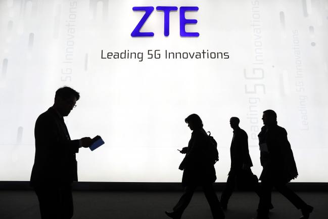© Bloomberg. Attendees pass by the ZTE Corp. stand during the opening day of the Mobile World Congress (MWC) in Barcelona, Spain, on Monday, Feb. 26, 2018.