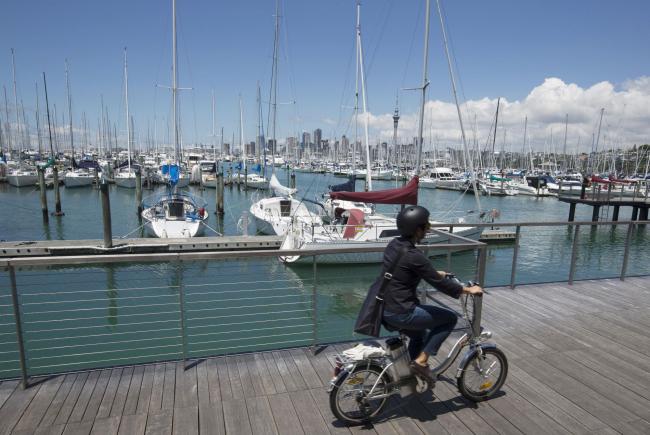 © Bloomberg. A woman rides a bicycle past yachts docked at a marina in Auckland, New Zealand, on Friday, Dec. 9, 2016. New Zealand last week unveiled a half-year budget update that forecast rising surpluses and a stronger economy than previously expected, giving prime minister Bill English the option of taking a tax-cuts package into next year's election campaign. Photographer: Brendon O'Hagan/Bloomberg