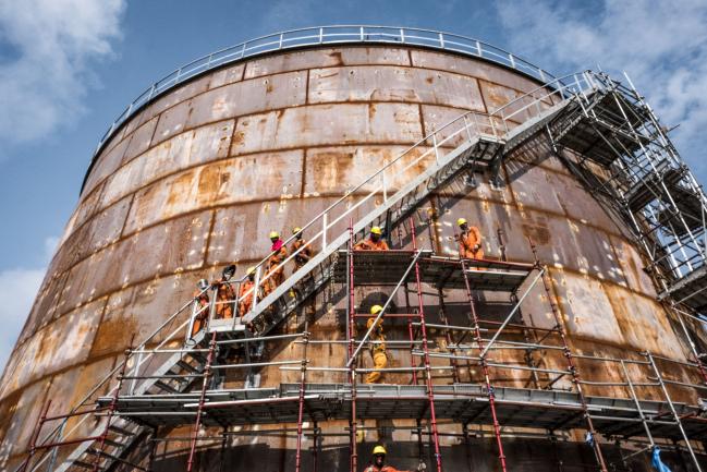 © Bloomberg. Workers climb scaffolding surrounding a storage tank at the under-construction Dangote Industries Ltd. oil refinery and fertilizer plant site in the Ibeju Lekki district, outside of Lagos, Nigeria, on Thursday, July 5, 2018. The $10 billion refinery, set to be one of the world’s largest and process 650,000 barrels of crude a day, should be near full capacity by mid-2020, Devakumar Edwin, group executive director at Dangote Industries said in an interview. Photographer: Tom Saater/Bloomberg