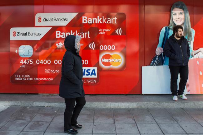 © Bloomberg. A pedestrian passes an advertisement for TC Ziraat Bankasi AS bank cards, using Visa Inc. and Mastercard Inc. payment services, on a street in the Levent district of Istanbul, Turkey. 