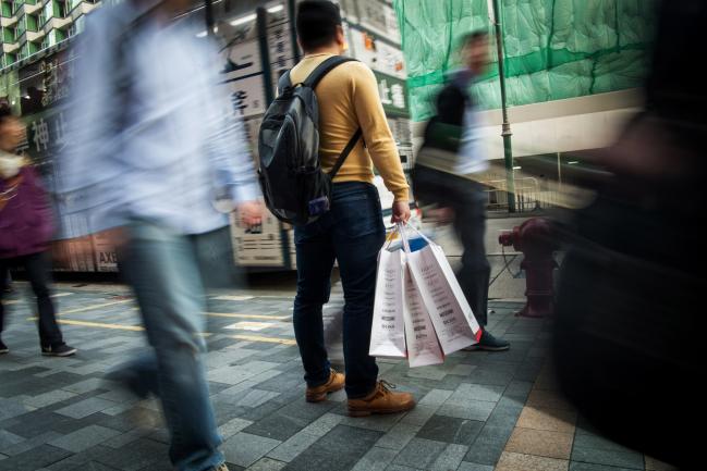 © Bloomberg. A pedestrian carrying shopping bags stands along a road in Hong Kong, China, on Saturday, Dec. 9, 2017. With more Chinese tourists likely to travel to Hong Kong next year as the yuan strengthens against the Hong Kong dollar, retailers are poised to benefit from the rise in store sales and falling rents, according to Catherine Lim, an analyst at Bloomberg Intelligence.