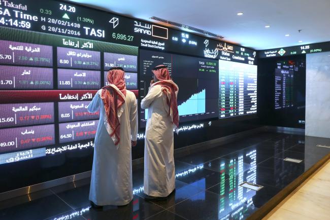 © Bloomberg. Visitors stand and watch stock movements displayed on large video screens inside the Saudi Stock Exchange, also known as the Tadawul All Share Index in Riyadh, Saudi Arabia. Photographer: Simon Dawson/Bloomberg