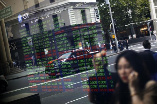 © Bloomberg. Pedestrians are reflected in a window as they walk past an electronic stock board at the ASX Ltd. exchange centre in Sydney, Australia, on Thursday, Feb. 14, 2019. “We made good progress on our core initiatives across the period, including the program to replace CHESS with distributed ledger technology; upgrade of our secondary data centre to strengthen market resilience; and restructure of our Listings Compliance team to enhance the quality of market oversight,” ASX Chief Executive Officer Dominic Stevens said. Photographer: David Moir/Bloomberg