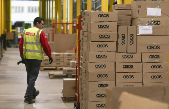 © Bloomberg. A worker wears a Norbert Dentressangle SA branded Hi-Vis safety jacket as he passes boxes of completed orders at Asos Plc's distribution warehouse in Barnsley, U.K. Photographer: Chris Ratcliffe/Bloomberg