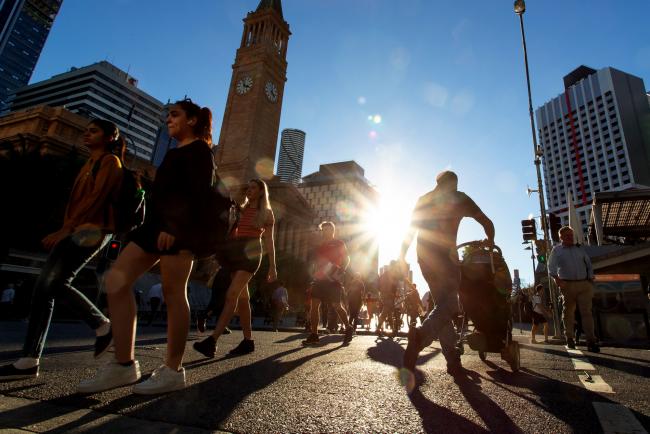 © Bloomberg. Pedestrians cross an intersection in Brisbane, Australia, on Tuesday, May 7, 2019. Australian central bank chief Philip Lowe dashed expectations of an interest-rate cut, looking through recent weakness in inflation to hitch the policy outlook to a labor market that he says remains strong. 