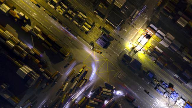 © Bloomberg. Light trails left by trucks run past containers sitting stacked at the Yangshan Deepwater Port, operated by Shanghai International Port Group Co. (SIPG), at night in this aerial photograph taken in Shanghai, China on Wednesday, Jan. 30, 2019.  Photographer: Qilai Shen/Bloomberg