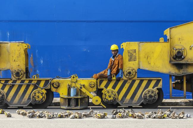 © Bloomberg. A worker sits under a gantry crane at the Jawaharlal Nehru Port, operated by Jawaharlal Nehru Port Trust (JNPT), in Navi Mumbai, Maharashtra, India, on Saturday, Dec. 16, 2017. Many of the cargo containers passing through India's busiest port in Mumbai have a small piece of Japan Inc. attached: Devices from NEC Corp. that can be tracked as the containers rumble through the interior of Asia's third-largest economy. 