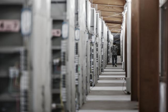 © Bloomberg. A technician walks past shelves containing bitcoin mining machines in Ordos, Inner Mongolia, China.