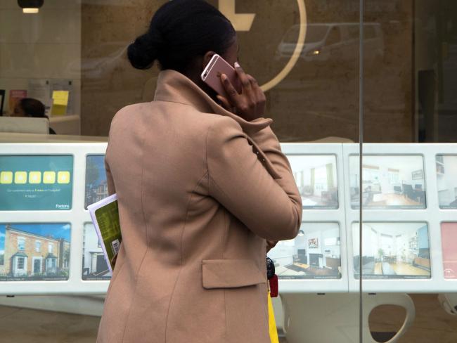 © Bloomberg. A woman speaks on her mobile phone while browsing properties displayed in the window of an estate agent in the Hackney borough of London, U.K. 