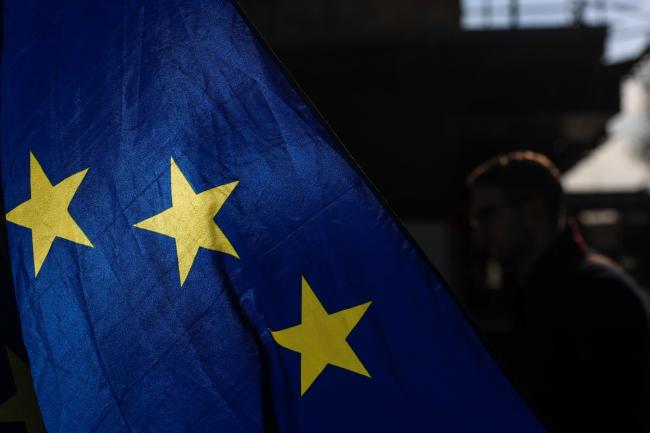 © Bloomberg. Sunlight illuminates the stars on a European Union (EU) flag near the Houses of Parliament in London, U.K., on Thursday, April 11, 2019. Brexit is on course to be delayed until the end of October under a plan to avoid a chaotic no-deal split, risking six more months of political uncertainty over Britain's ties to the European Union. Photographer: Simon Dawson/Bloomberg