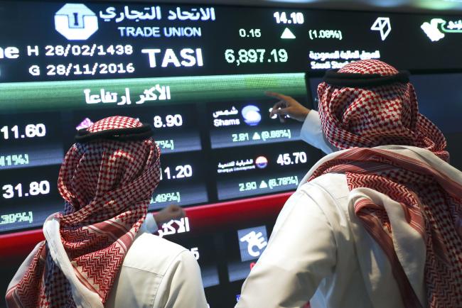 © Bloomberg. Visitors stand and watch stock movements displayed on large video screens inside the Saudi Stock Exchange, also known as the Tadawul All Share Index in Riyadh, Saudi Arabia, on Monday, Nov.28, 2016. The Tadawul All Share Index advanced 26 percent since Saudi Arabia’s record-breaking bond sale last month, the most in the world during that period. Photographer: Simon Dawson/Bloomberg