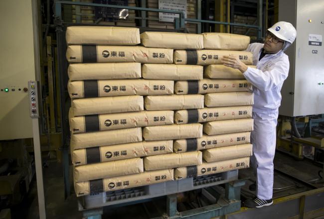 © Bloomberg. A Tofuku Flour Mills Co. employee moves a bag of flour for ramen noodles at the company's warehouse in Dazaifu, Fukuoka, Japan, on Dec. 21, 2017. Fukuoka, on Japan’s southern island of Kyushu, is expanding production of a locally-developed variety of grain known as Ra-Mugi that’s designed to be perfect for tonkotsu ramen: a dish of cloudy white pork broth, with noodles and slices of pork that originates in the region.