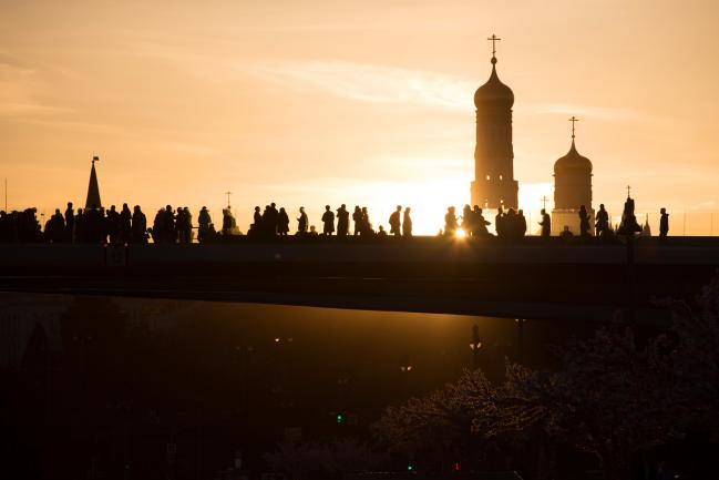 © Bloomberg. Visitors walk along the 'floating bridge' in Zaryadye park during sunset to view the Kremlin towers in Moscow, Russia, on Monday, April 9, 2018. Russia’s currency extended its plunge, dropping to the weakest level since Dec. 2016, as investors weighed the implications of the toughest U.S. sanctions yet.