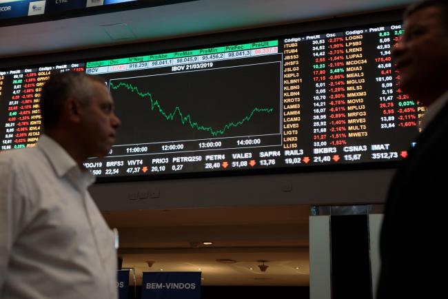 © Bloomberg. People pass by an electronic board displaying stock activity at the Brasil Bolsa Balcao (B3) stock exchange in Sao Paulo, Brazil, on Thursday, March 21, 2019. Brazil's Ibovespa Index fell Thursday following the arrest of former Brazilian president Michel Temer as part of the Carwash corruption probe that's ensnared some of the country's top business executives and politicians. 