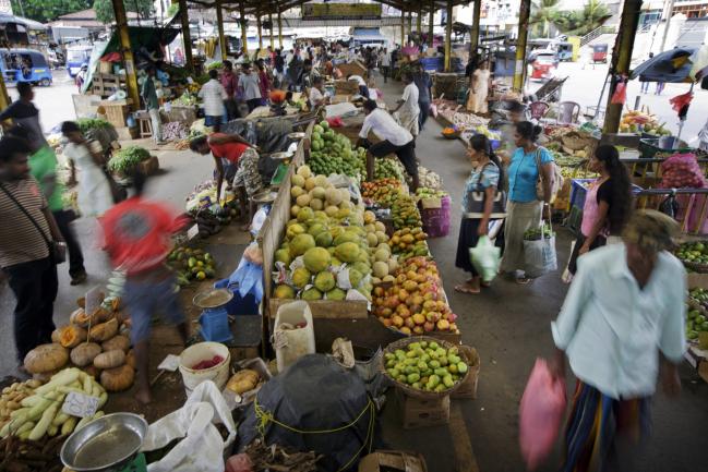 © Bloomberg. Customers shop at a fruit and vegetables stall at a market in the Pettah area of Colombo, Sri Lanka, on Sunday, July 19, 2015.  