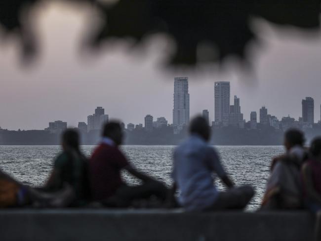 © Bloomberg. People sit on the waterfront as commercial and residential buildings stand in the background in the Nariman Point area of Mumbai. Photographer: Dhiraj Singh/Bloomberg