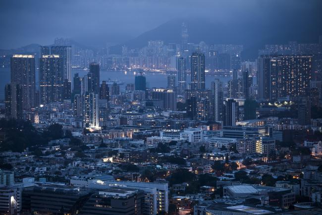 © Bloomberg. Residential buildings stand illuminated at dusk in Hong Kong, China, on Saturday, June 3, 2017. Hong Kong’s de facto central bank has placed restrictions on bank borrowing for construction and land purchases. That will affect many mainland Chinese developers who take on more debt than local firms to buy land, but it’s unlikely to stop the trend of local developers losing out to Chinese firms. Photographer: Justin Chin/Bloomberg