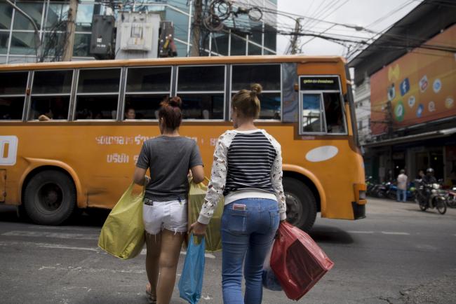 © Bloomberg. Shoppers carrying bags cross a street in Bangkok, Thailand, on Saturday, Oct. 21, 2017. Thai household consumption, worth about half the country's $407 billion gross domestic product, has been subdued amid a yearlong mourning period for late King Bhumibol Adulyadej that ends on Oct. 29. 