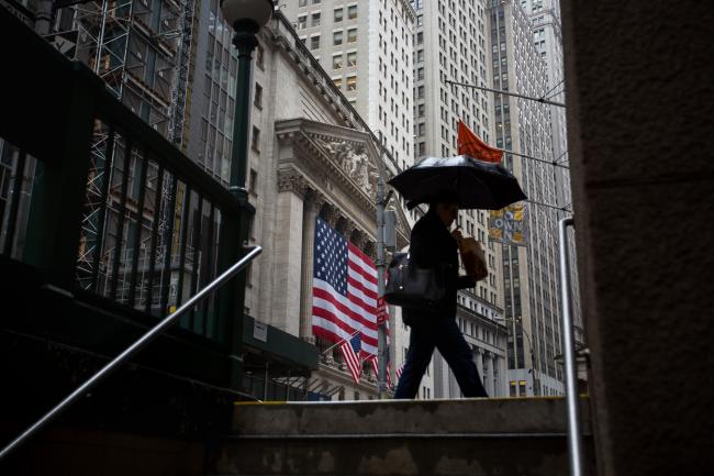 © Bloomberg. A pedestrian holds an umbrella while walking past the New York Stock Exchange (NYSE) in New York, U.S., on Monday, Nov. 13, 2017. U.S. stocks fluctuated, while Treasuries and the dollar edged higher as investors awaited clues on the direction of monetary policy and tax reform.