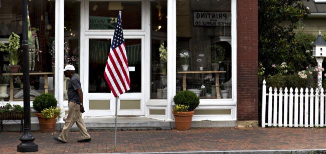 © Bloomberg. A pedestrian walks past an American flag on Main Street in Smithfield, Virginia. Photographer: Andrew Harrer/Bloomberg
