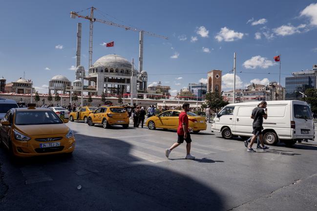 © Bloomberg. Pedestrians pass construction works at the Taksim mosque on Taksim Square in Istanbul, Turkey, on Monday, Aug. 13, 2018. Turkish policy makers made their first move to bolster the financial system and investor confidence amid a plunge in the lira. The currency, stocks and bonds extended their decline. 