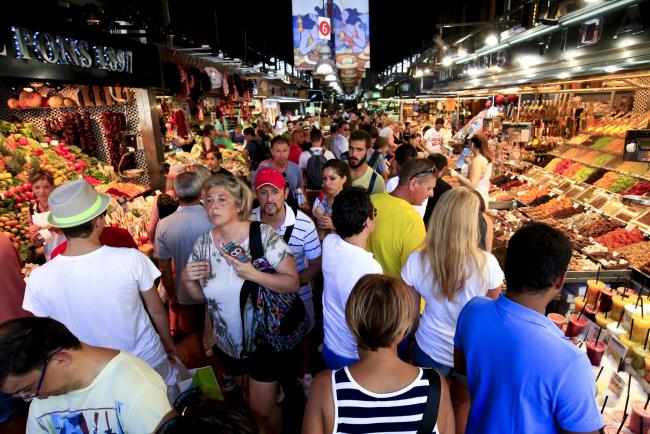 © Bloomberg. Tourists and pedestrians fill an aisle between food stalls inside Boqueria market in Barcelona, Spain. Photographer: Pau Barrena