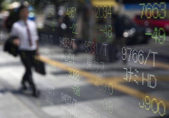 © Bloomberg. A pedestrian is reflected in an electronic stock board outside a securities firm in Tokyo, Japan, on Friday, July 29, 2016. Shares in Tokyo fluctuated as investors weighed the Bank of Japans decision to expand exchange-traded fund purchases while keeping its bond-buying program and interest rates unchanged.