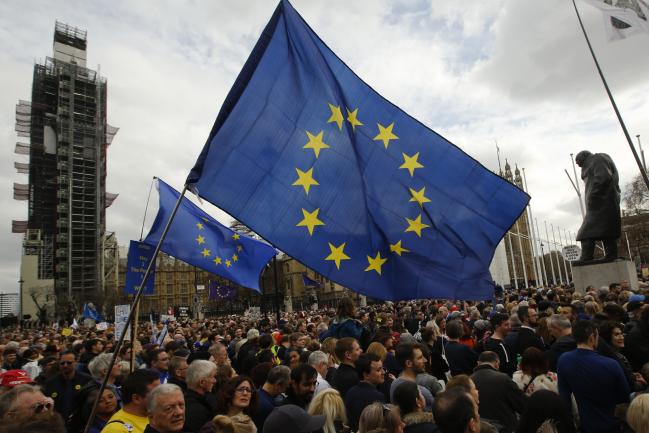 © Bloomberg. Demonstrators wave large European Union (EU) flags as they stand on Parliament Square during the anti-Brexit People's Vote rally in London, U.K., on Saturday, March 23, 2019. The campaign to give U.K. citizens a vote on U.K. Prime Minister Theresa May's Brexit deal, twice defeated by Parliament, holds the rally after European Union leaders gave May an extra two weeks to work out what to do. Photographer: Luke MacGregor/Bloomberg