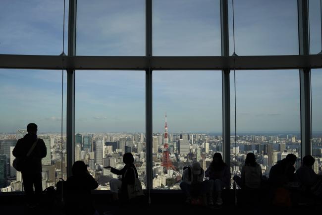 © Bloomberg. Visitors look out from the observation deck of the Roppongi Hills Mori Tower, operated by Mori Building Co., in Tokyo, Japan, on Monday, March 18, 2019. Amid intense debate on Japan’s inflation target, some officials at the central bank think the 2 percent goal will probably remain out of reach for the next three years, according to people familiar with the matter. Photographer: Toru Hanai/Bloomberg