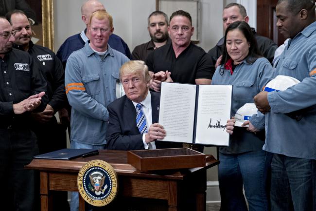 © Bloomberg. U.S. President Donald Trump holds up a signed proclamation on adjusting imports of steel into the United States next to steel and aluminum workers in the Roosevelt Room of the White House in Washington, D.C., U.S.