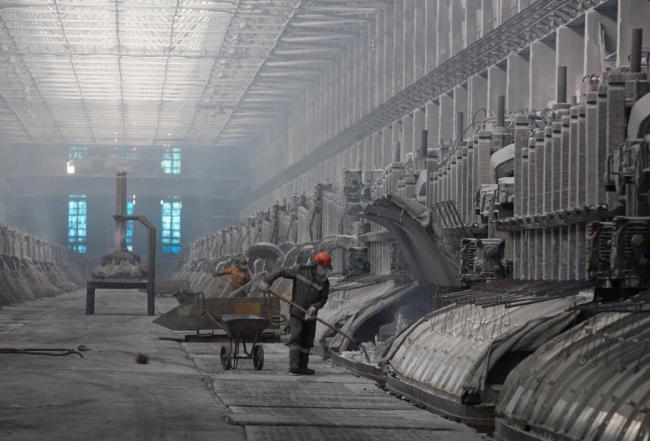 © Bloomberg. A worker uses a shovel to move material in an electrolysis bath in the electrolysis shop at the Sayanogorsk aluminium smelter, operated by United Co. Rusal, in Sayanogorsk, Russia.