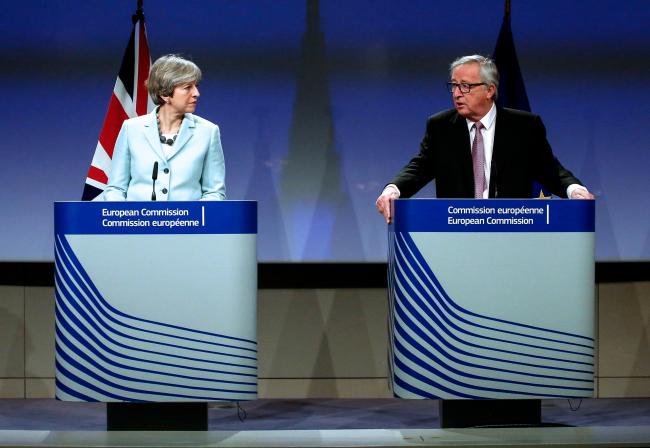 © Bloomberg. Theresa May, U.K. prime minister, left, looks on as Jean-Claude Juncker, president of the European Commission, speaks during a news conference at the European Commission building in Brussels, Belgium, on Friday, Dec. 8, 2017. The U.K. and the European Union struck a deal to unlock divorce negotiations, opening the way for talks on what businesses are keenest to nail down -- the nature of the post-Brexit future.