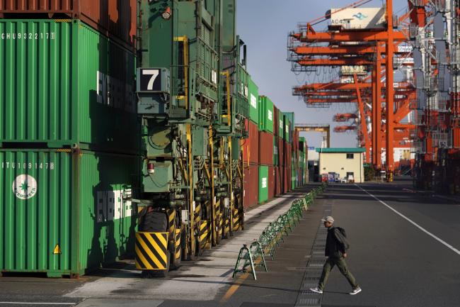 © Bloomberg. A man walks towards shipping containers stacked at a terminal in Tokyo, Japan, on Monday, April 15, 2019. Japan’s chief negotiator dodged questions about any potential auto export penalties or currency clause as he emerged from the first day of long-awaited trade talks with the U.S. in Washington, D.C., U.S., on April 15. Photographer: Toru Hanai/Bloomberg