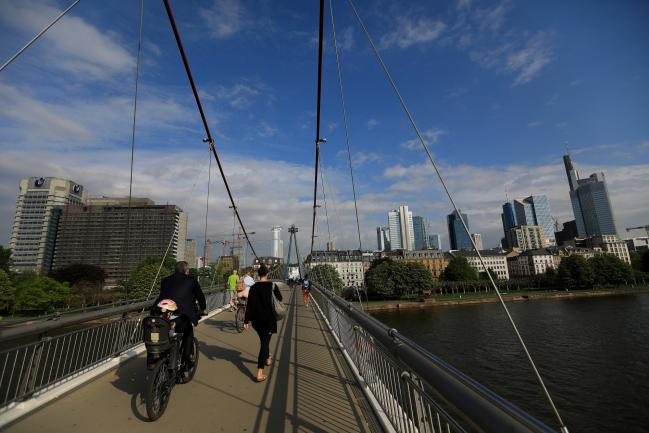 © Bloomberg. A cyclist and pedestrians pass over a bridge spanning the River Main as skyscrapers stand beyond in Frankfurt, Germany, on Wednesday, April 25, 2018. About 8,000 additional jobs may be created in Frankfurt’s banking industry, a statement from the Government of Hesse state says, citing estimates by Helaba Research. Photographer: Krisztian Bocsi/Bloomberg