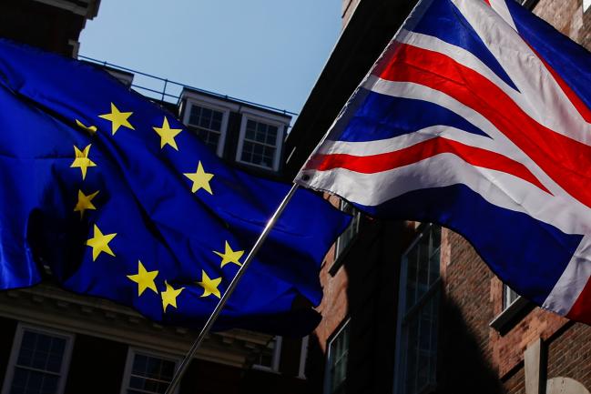 © Bloomberg. Campaigners wave an European Union (EU) flag and a Union flag, also known as a Union Jack, during an anti-Brexit demonstration outside the Conservative Party general-election campaign headquarters in London, U.K., on Friday, May 26, 2017. Brexit SecretaryDavid Davissaid European Union demands to protect its citizens' rights in the U.K. are 