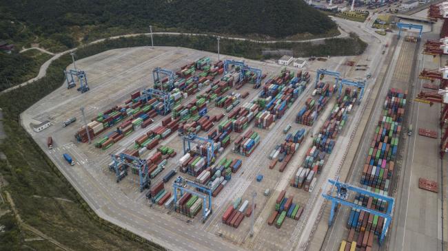 © Bloomberg. Containers sit stacked next to gantry cranes in this aerial photograph taken above the Port of Ningbo-Zhoushan in Ningbo, China. Photographer: Qilai Shen/Bloomberg